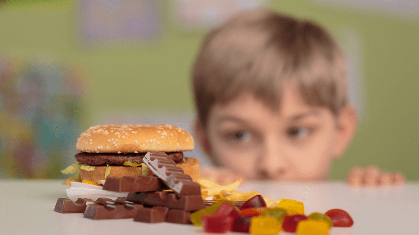 Хлопчик дивиться на бургер, шоколад та цукерки